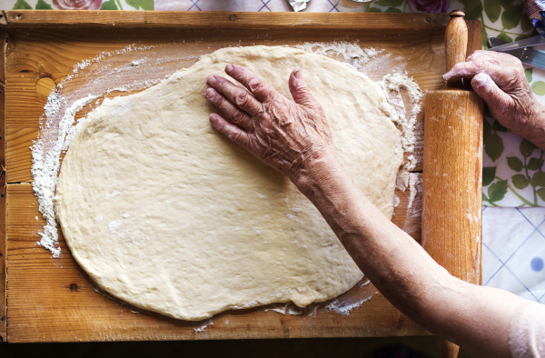 Senior woman baking pies in her home kitchen. Rolling dough using rolling pin.