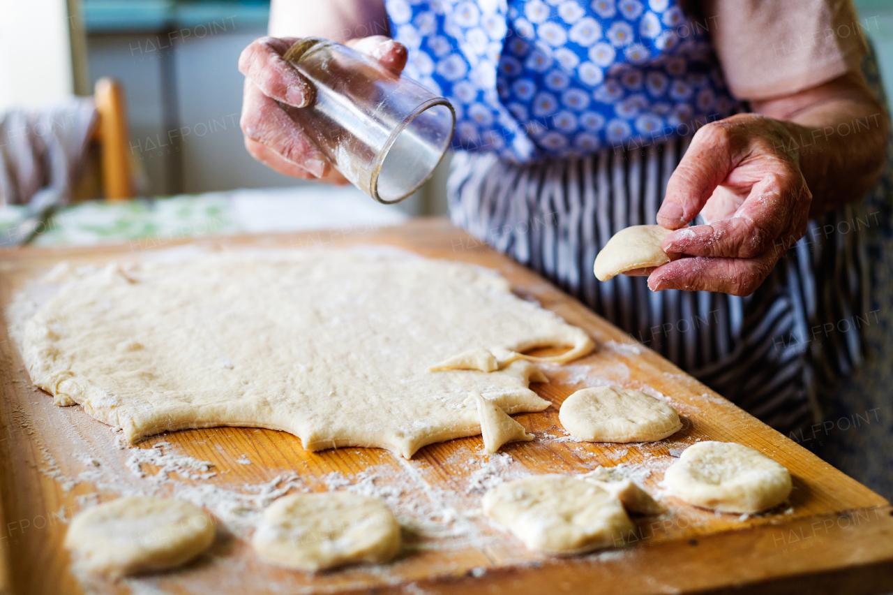 Senior woman baking pies in her home kitchen. Cutting out circles from raw dough.