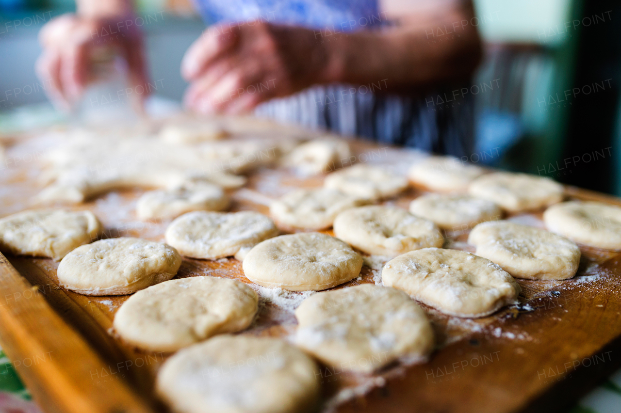 Senior woman baking pies in her home kitchen. Cutting out circles from raw dough.