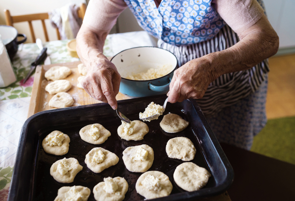 Senior woman baking pies in her home kitchen. Filling the buns with cottage cheese.