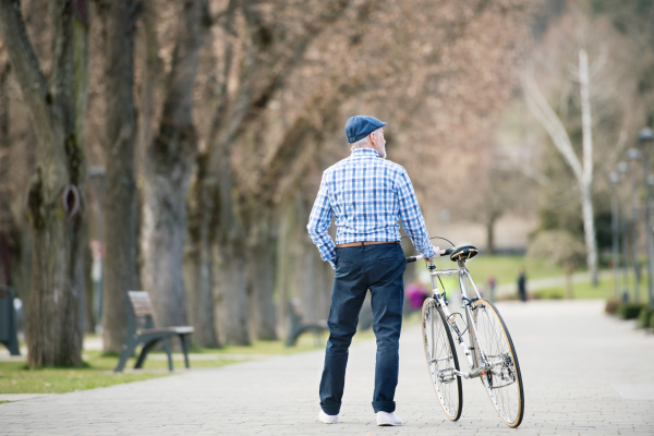 Handsome senior man in blue checked shirt with bicycle in town. Sunny spring day. Rear view.