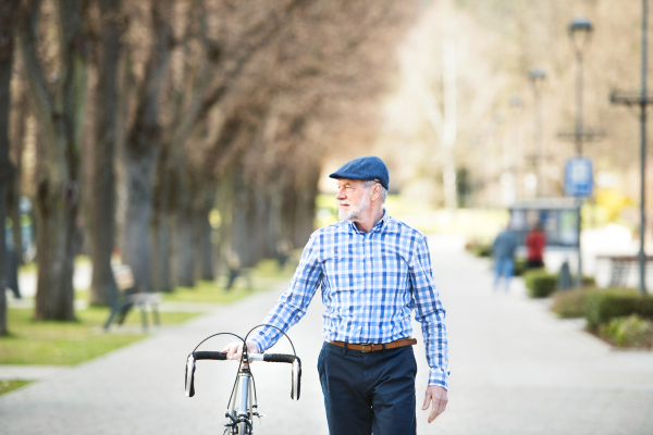 Handsome senior man in blue checked shirt with bicycle in town. Sunny spring day.