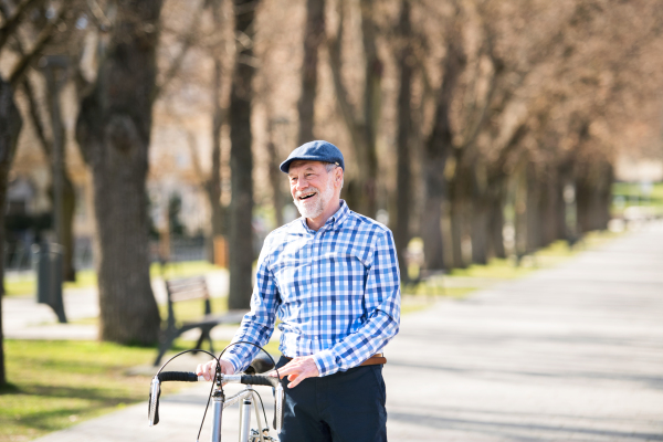 Handsome senior man in blue checked shirt with bicycle in town. Sunny spring day.