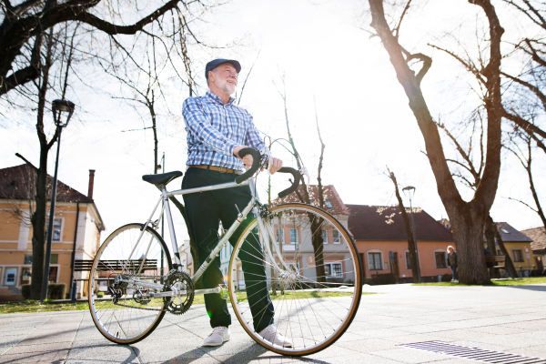 Handsome senior man in blue checked shirt with bicycle in town, looking up. Sunny spring day.