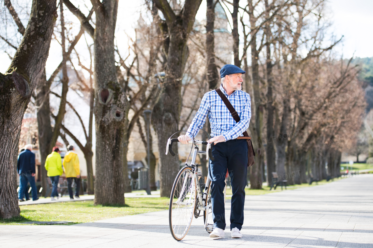 Handsome senior man in blue checked shirt with bicycle in town, looking up. Sunny spring day.