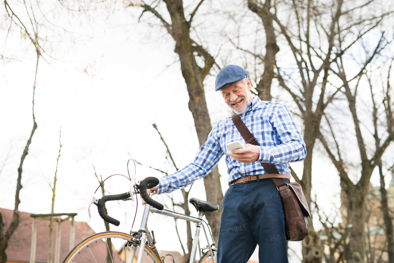 Handsome senior man in blue checked shirt with bicycle in town holding smart phone, texting.