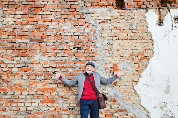 Handsome senior man in gray jacket holding smart phone. Orange brick wall background.