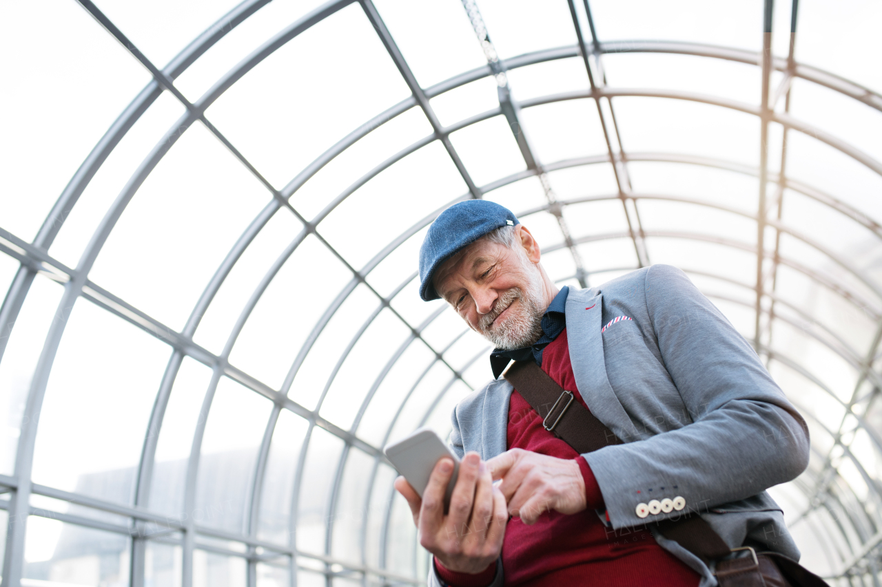 Handsome senior man in gray jacket holding smart phone, texting. Glass ceiling background.