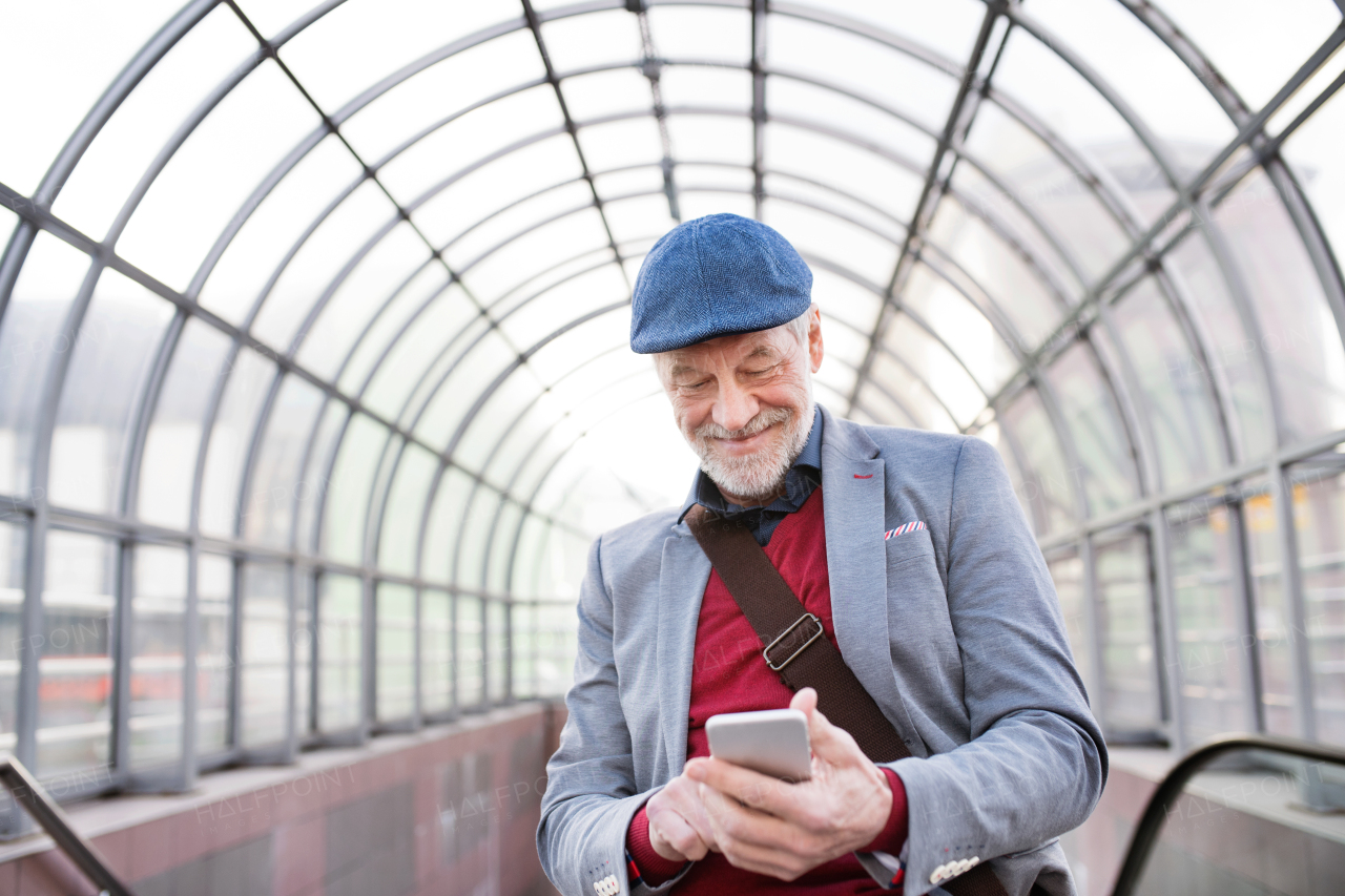 Handsome senior man in gray jacket holding smart phone, texting. Glass ceiling background.