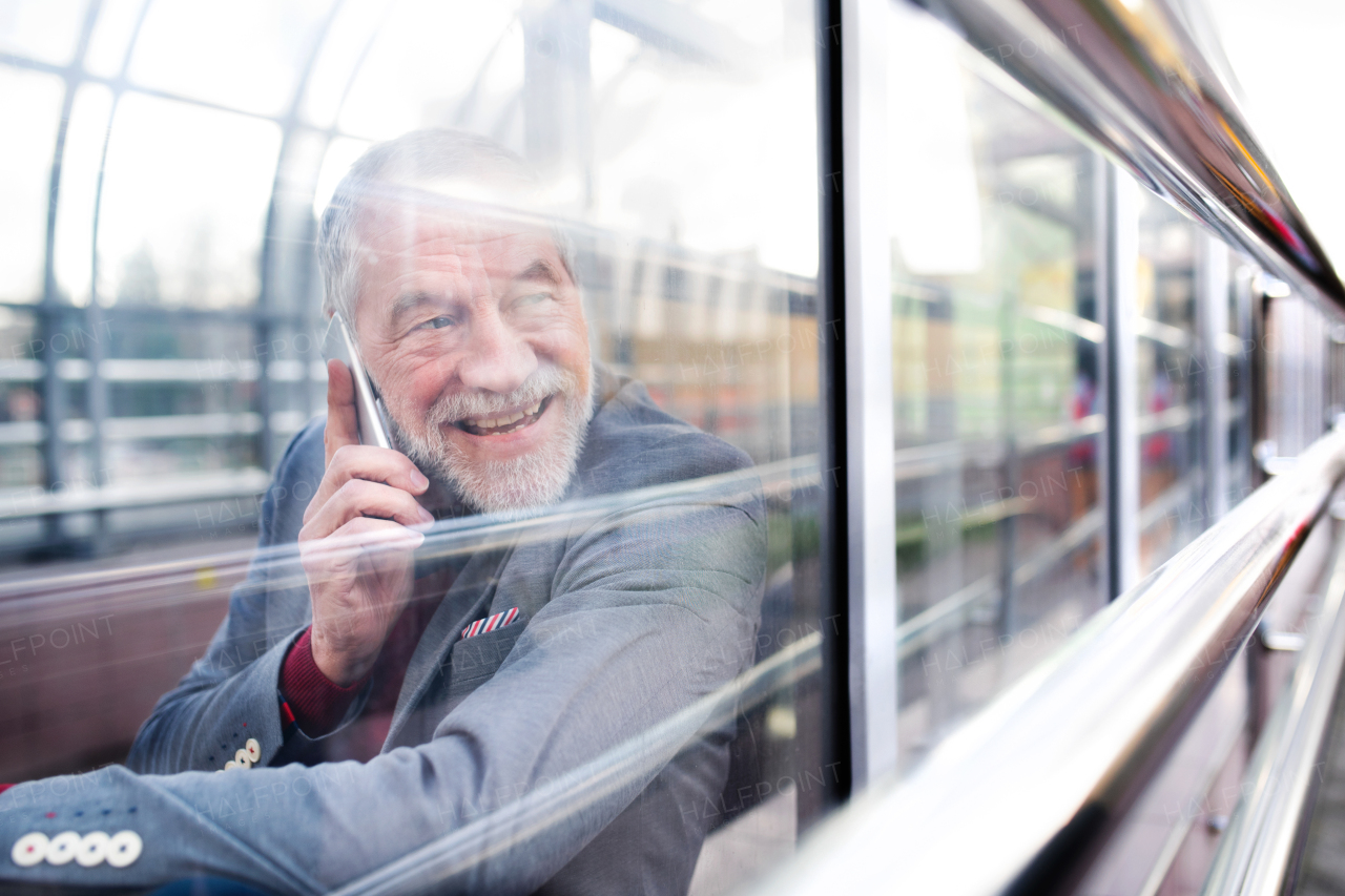 Handsome senior man in gray jacket holding smart phone making phone call. View through glass.