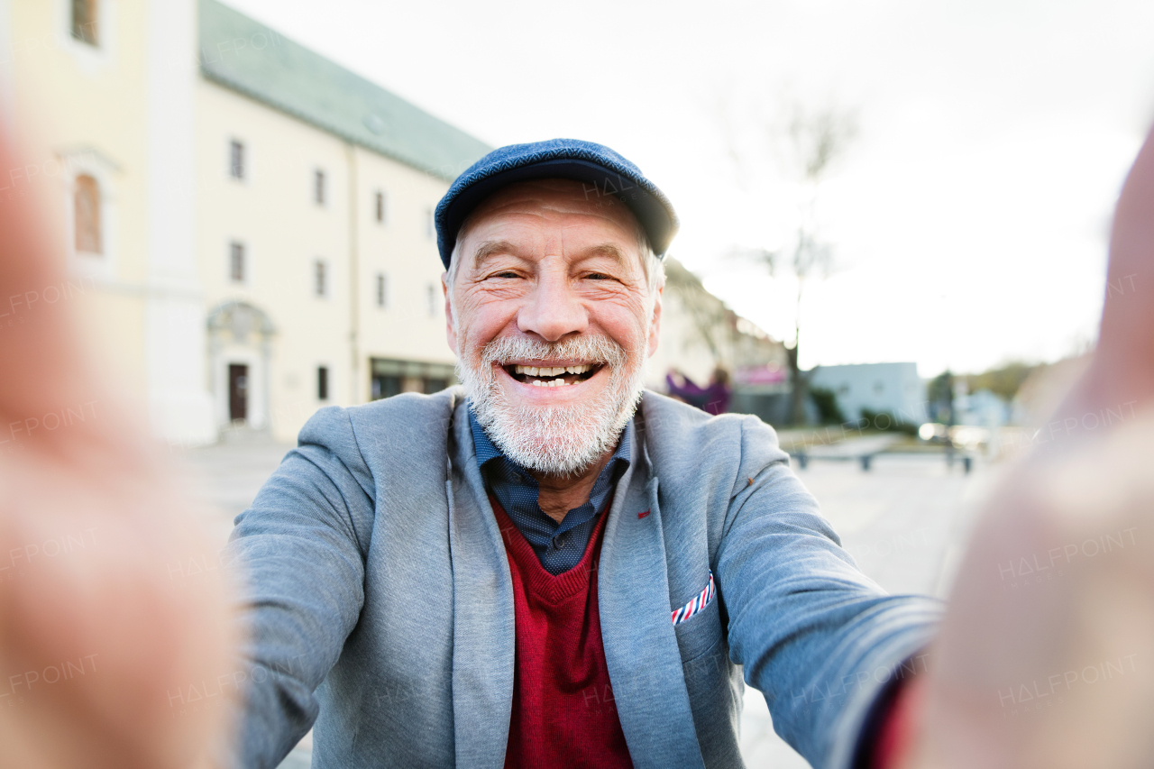 Handsome senior man in gray jacket and flat cap in town taking selfie of himself.