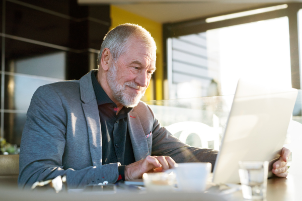 Handsome senior businessman working on laptop in cafe. Sunny spring day.