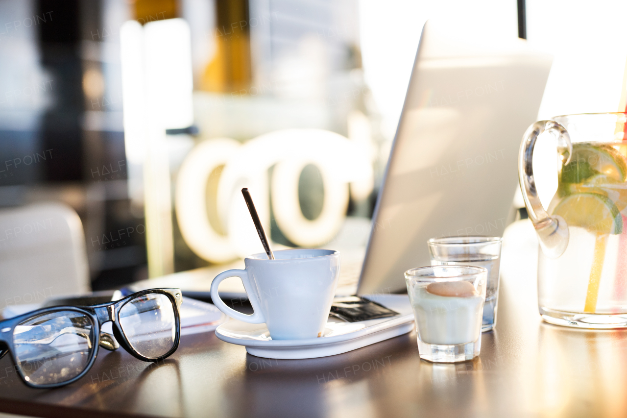 Coffee cup, water glass, lemonade, eyeglasses and laptop laid on table in cafe.