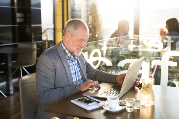 Handsome senior businessman working on laptop in cafe. Sunny spring day.