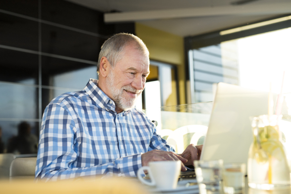 Handsome senior businessman working on laptop in cafe. Sunny spring day.