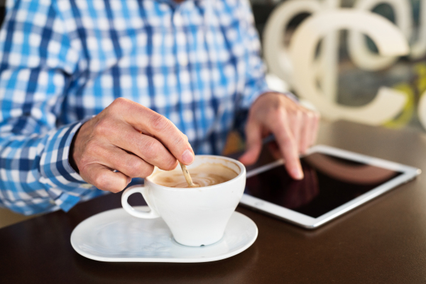 Unrecognizable senior businessman working on tablet in cafe. Sunny spring day.