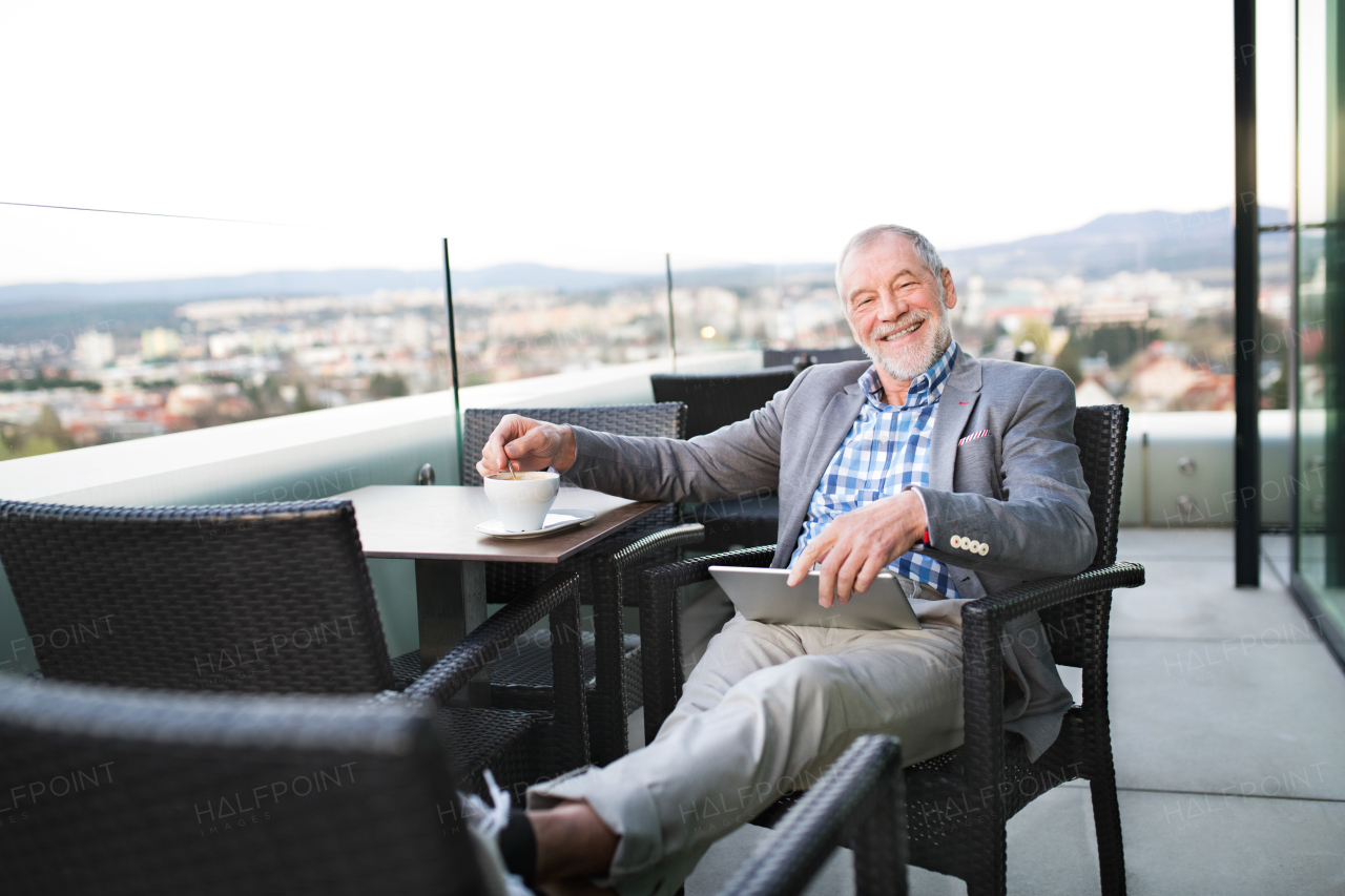 Handsome senior businessman working on tablet and enjoying coffee with his feet up in rooftop cafe. Sunny spring day.