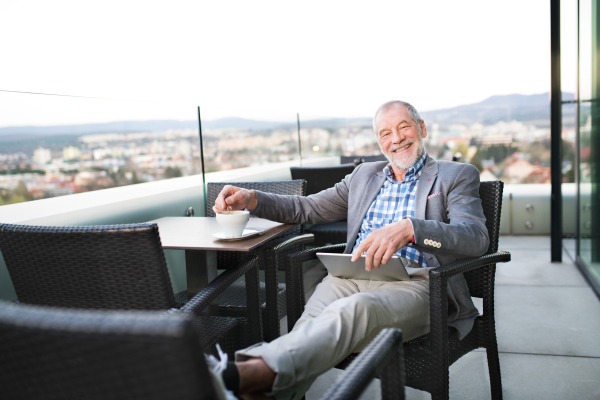 Handsome senior businessman working on tablet and enjoying coffee with his feet up in rooftop cafe. Sunny spring day.