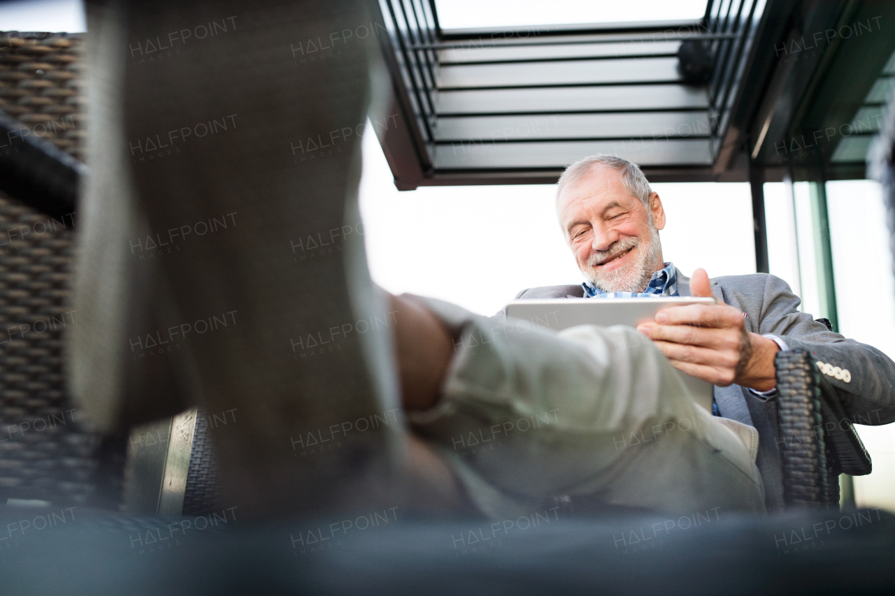 Handsome senior businessman working on tablet with his feet up in rooftop cafe. Sunny spring day.