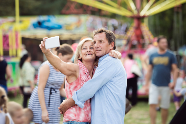 Senior couple having a good time at the fun fair, taking selfie with smart phone