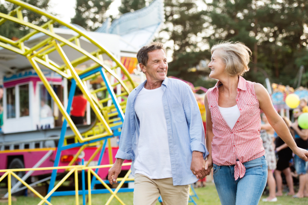 Senior couple having a good time at the fun fair, holding hands, running. Sunny summer day.