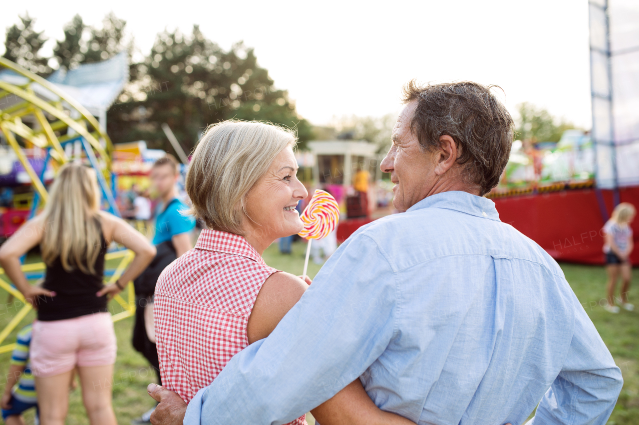 Senior couple having a good time at the fun fair, hugging. Woman holding lollipop. Rear view.