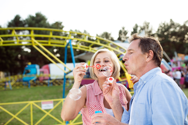 Senior couple having a good time at the fun fair, blowing soap bubbles with bubble wand.