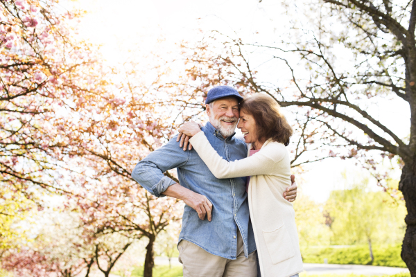 Beautiful senior couple in love on a walk outside, enjoying spring nature under blossoming trees. Man and woman having fun.