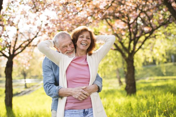 Beautiful senior couple in love on a walk outside in spring nature under blossoming trees.