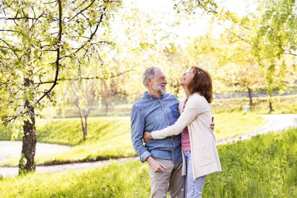 Beautiful senior couple in love on a walk outside, enjoying spring nature under blossoming trees. Man and woman having fun.