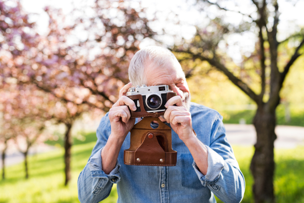 Senior man outside in spring nature taking pictures with a camera.