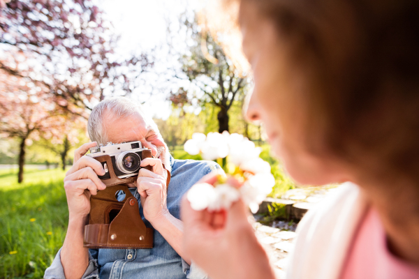 Beautiful senior couple in love outside in spring nature. Man with camera taking a picture of a woman.