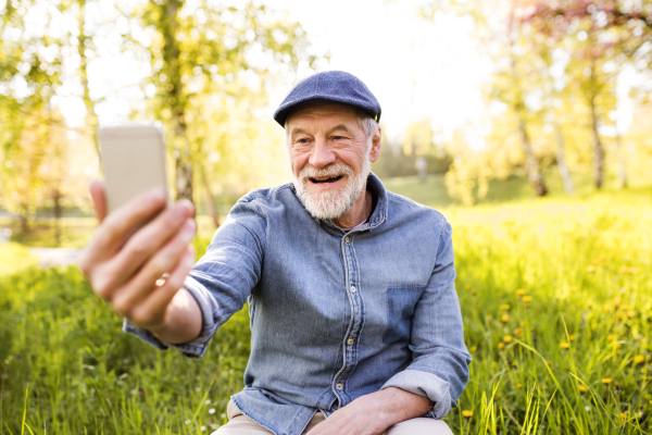 Senior man taking a selfie with smartphone outside in spring nature.