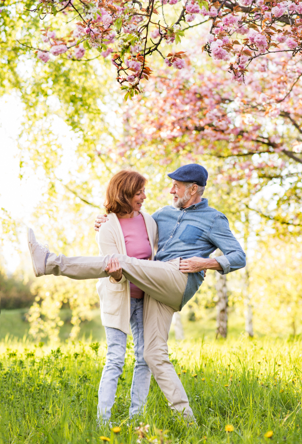 Beautiful senior couple in love on a walk outside, enjoying spring nature under blossoming trees. Man and woman having fun.