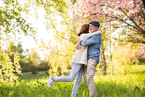 Beautiful senior couple in love on a walk outside, enjoying spring nature under blossoming trees. Man and woman having fun.