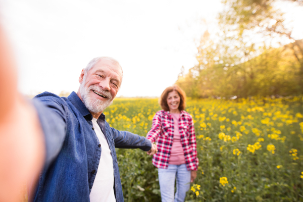 Beautiful senior couple in love on a walk outside in spring nature. Man and woman taking a selfie with a smartphone.