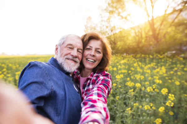 Beautiful senior couple in love on a walk outside in spring nature. Man and woman taking a selfie with a smartphone.