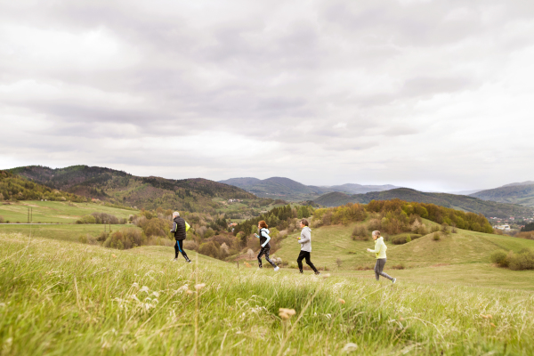 Group of active seniors running together outside on the green hills.