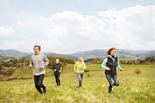 Group of active seniors running together outside on the green hills.