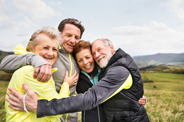 Group of active senior runners outdoors, resting and hugging in windy cold weather.