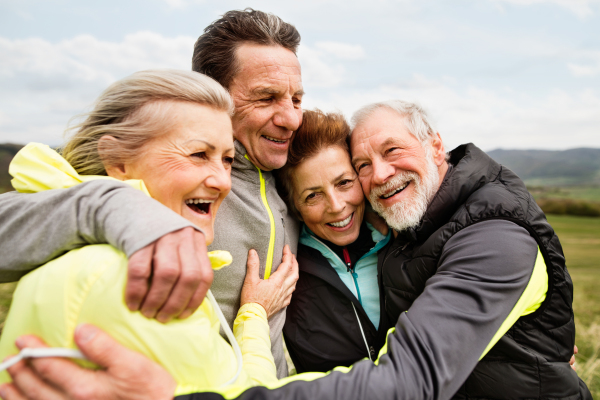 Group of active senior runners outdoors, resting and hugging in windy cold weather.