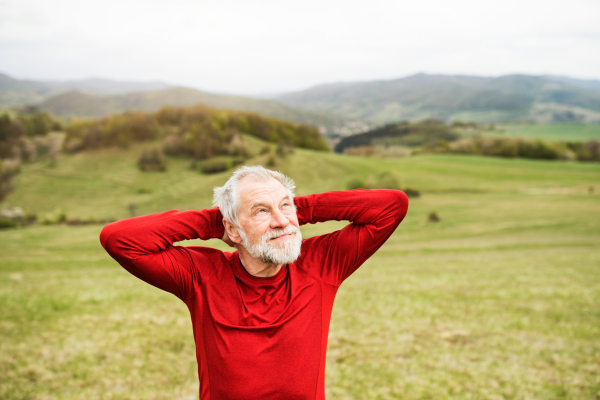 Active senior runner in red sweatshirt outside on green hills, taking break, resting.