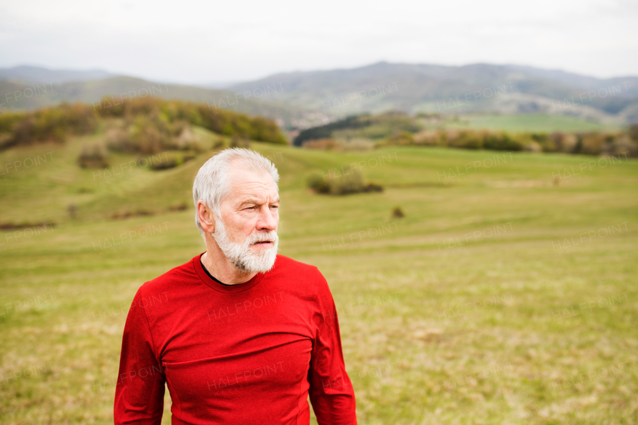 Active senior runner in red sweatshirt outside on green hills, taking break, resting.