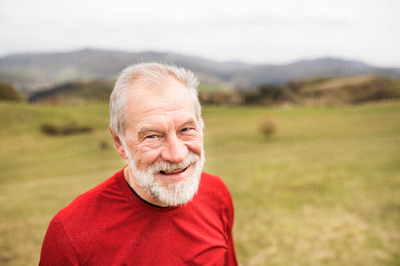 Active senior runner in red sweatshirt outside on green hills, taking break, resting.