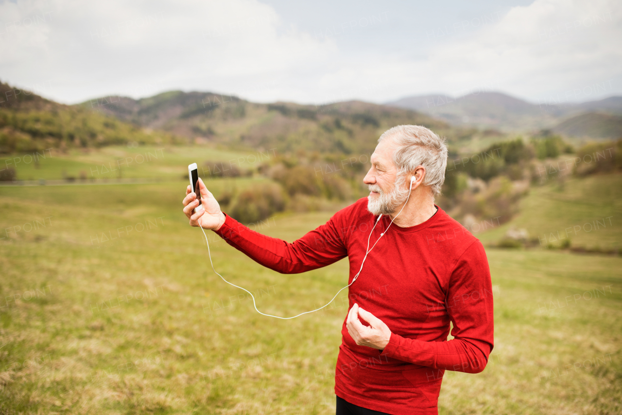 Active senior runner outside on the green hills taking selfie with smart phone.