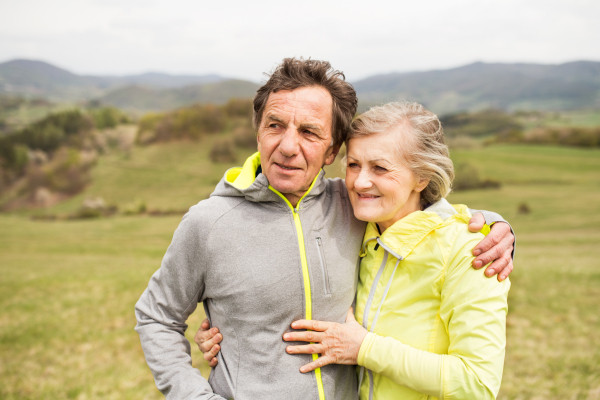 Beautiful active senior runners resting outside in sunny autumn nature, hugging.