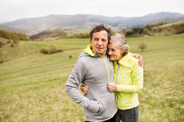 Beautiful active senior runners resting outside in sunny autumn nature, hugging.