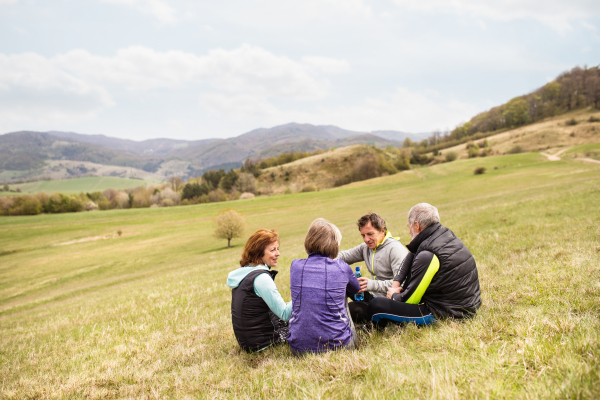 Group of active senior runners outdoors, sitting on the grass, resting and talking together.