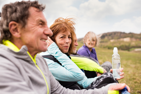 Group of active senior runners outdoors, sitting on the grass, resting and talking together.