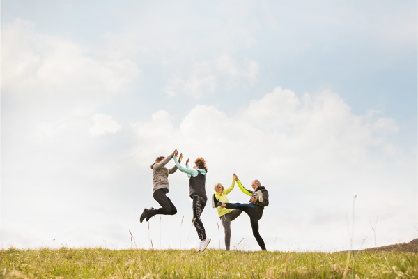 Group of active senior runners outdoors resting, holding hands, jumping and having fun.